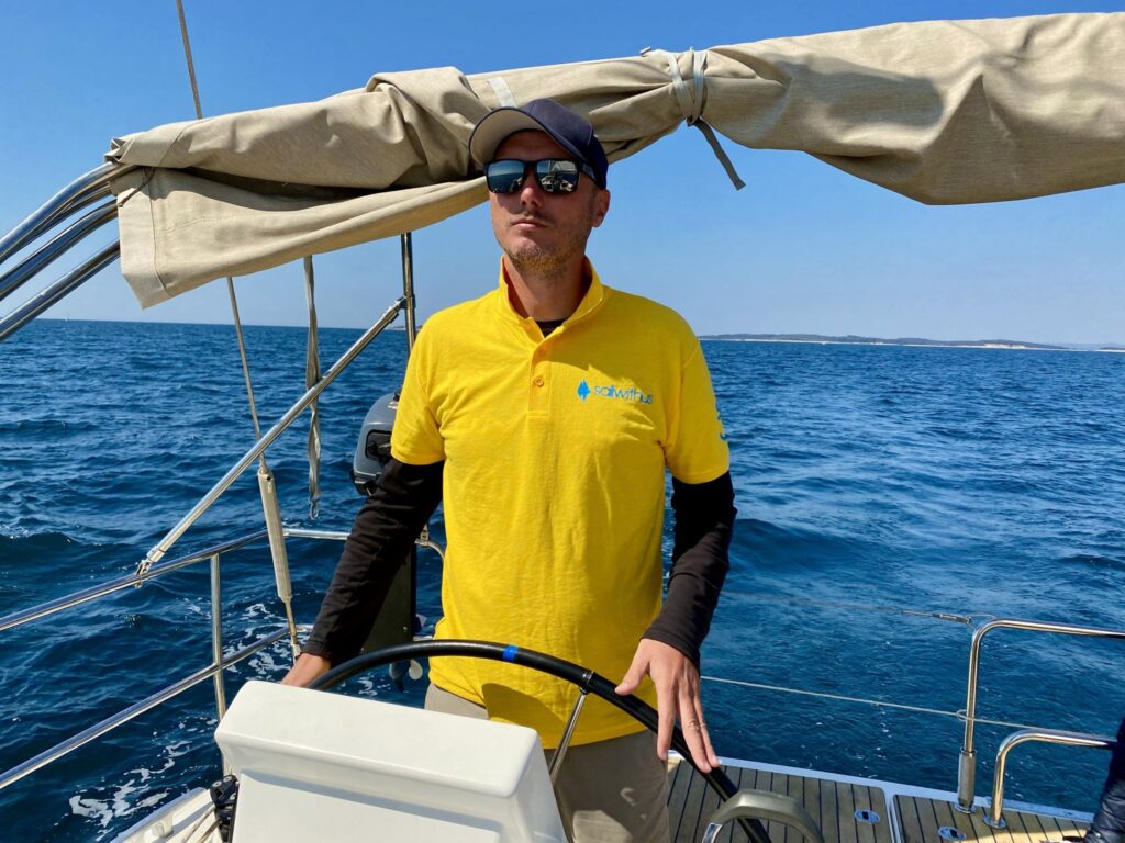 Skipper Carsten steuert ein Segelboot im Sailwithus-T-Shirt